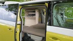 the interior of a van with its door open and seats folded down, in front of some trees