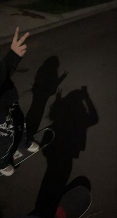 a person riding a skateboard on a street at night with the shadow of their hand