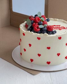 a white cake with berries and blueberries on top sits in front of a cardboard box