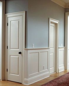 an empty room with white paneling and wood flooring on the walls, along with a red rug