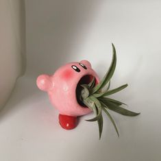 a pink toy with an air plant sticking out of it's mouth on a white surface