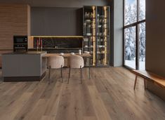 a modern kitchen with wood flooring and large windows overlooking the snow covered trees outside