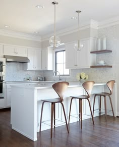 three chairs are sitting at the bar in this modern kitchen with white cabinets and wood flooring