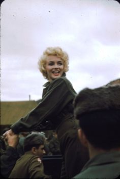 an old photo of a woman standing in front of some soldiers and smiling at the camera