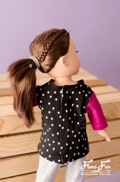 a doll wearing a black and white top with stars on it's sleeves, standing next to a wooden box