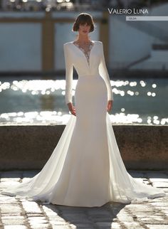 a woman in a white wedding dress standing by the water with her hands on her hips