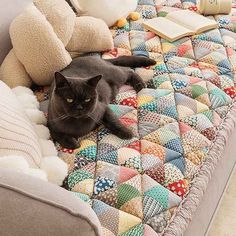 a black cat laying on top of a couch next to pillows and stuffed animal toys