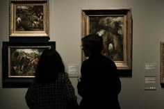 two people looking at paintings on display in a museum