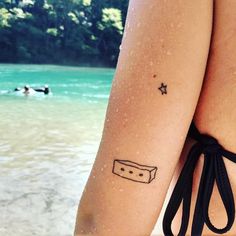 a woman with a tattoo on her arm standing in front of the water and people swimming