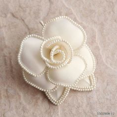 a white flower brooch with pearls on it's center sits on a piece of fabric