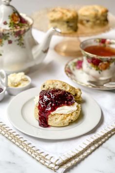 scones filled with jam and cream on a plate next to tea cups, saucers and spoons