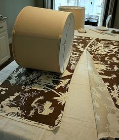 a roll of toilet paper sitting on top of a brown and white table cloth next to a lamp