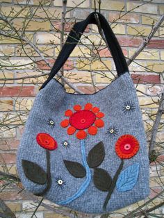 a gray bag with red flowers on it hanging from the side of a brick wall