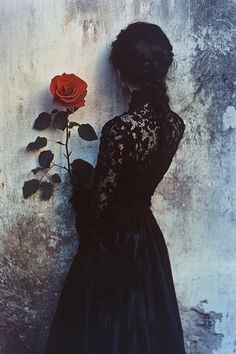 a woman in a black dress standing next to a wall with a red rose on it