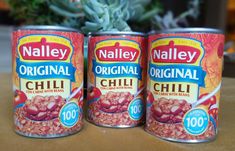 three cans of chili sitting on top of a table next to a succulent plant