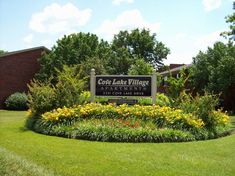 the sign for core lake village apartments is surrounded by flowers and grass in front of a brick building