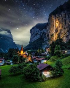 the night sky is lit up over a small village with mountains in the back ground