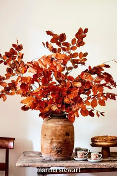 a vase filled with red leaves on top of a wooden table next to a plate