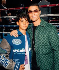 two men standing next to each other in front of a boxing ring with people watching