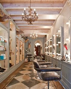 the interior of a hair salon with several chairs and mirrors on the wall, along with an ornate chandelier hanging from the ceiling