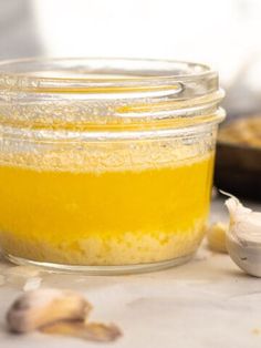 a jar filled with yellow liquid next to garlic