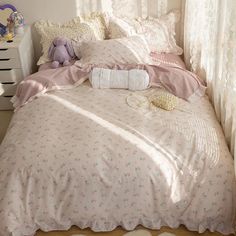 an unmade bed with pink and white comforter in a small room next to a window