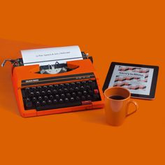 an orange typewriter next to a cup of coffee and a tablet on an orange background