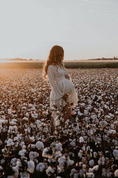 a pregnant woman standing in a cotton field at sunset with the sun setting behind her