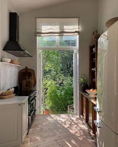 a kitchen with an open door leading to a forest outside the window, and wooden flooring