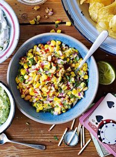 corn salad with guacamole and chips in bowls on a table next to playing cards