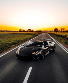 a black sports car is driving down the road at sunset or dawn with grass and trees in the background