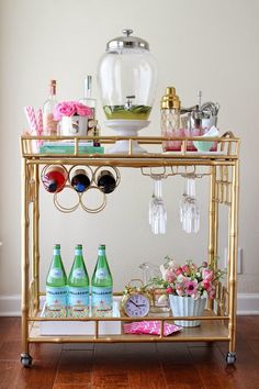 a gold bar cart filled with bottles and glasses on top of a hard wood floor