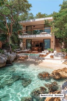 the house is surrounded by trees, rocks and clear blue water in front of it