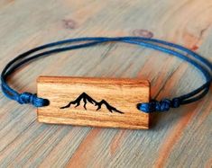 a wooden bracelet with mountains engraved on the front and blue string around it, sitting on a wood surface