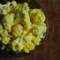 a glass bowl filled with cauliflower on top of a wooden table