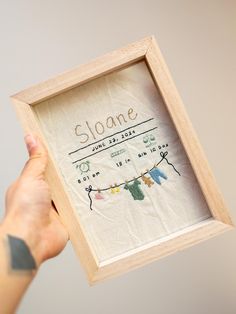 a person holding up a small wooden frame with clothes hanging from it's sides