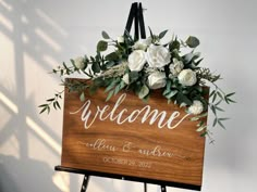 a welcome sign with white flowers and greenery on it is hanging from the wall