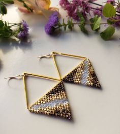 two pairs of gold and white triangle shaped earrings on a table with flowers in the background