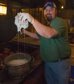 a man in green shirt and white gloves pouring something into a pot on top of a stove