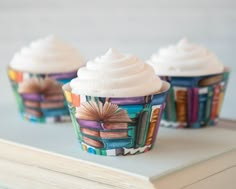 three cupcakes with white frosting on top of an open book sitting on a table