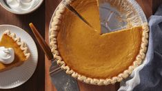 a pie with a slice missing from it on a wooden table next to plates and utensils