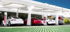 three electric cars parked in front of a gas station with green plants growing on the ground