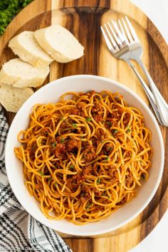 a bowl of spaghetti with meat and parmesan bread next to it on a cutting board