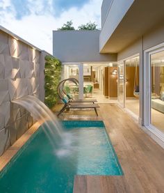 an indoor swimming pool with a waterfall and lounge chairs next to it, in front of a modern home