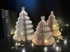 three christmas trees made out of book pages with lights on them and some books in the background