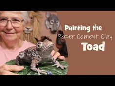 an older woman holding a frog on top of a green leafy surface with the words painting the paper cement toad