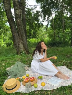 a woman is sitting on a blanket in the grass with fruits and books around her