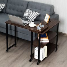 a laptop computer sitting on top of a wooden table next to a gray couch with black and white pillows