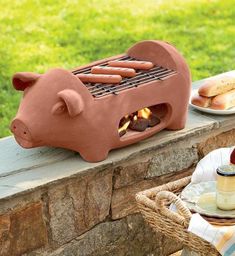 a pig shaped grill sitting on top of a stone wall next to a plate of food