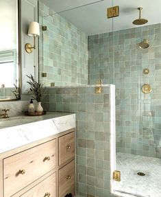 a bathroom with green tiled walls and gold hardware on the shower door, vanity sink and mirror